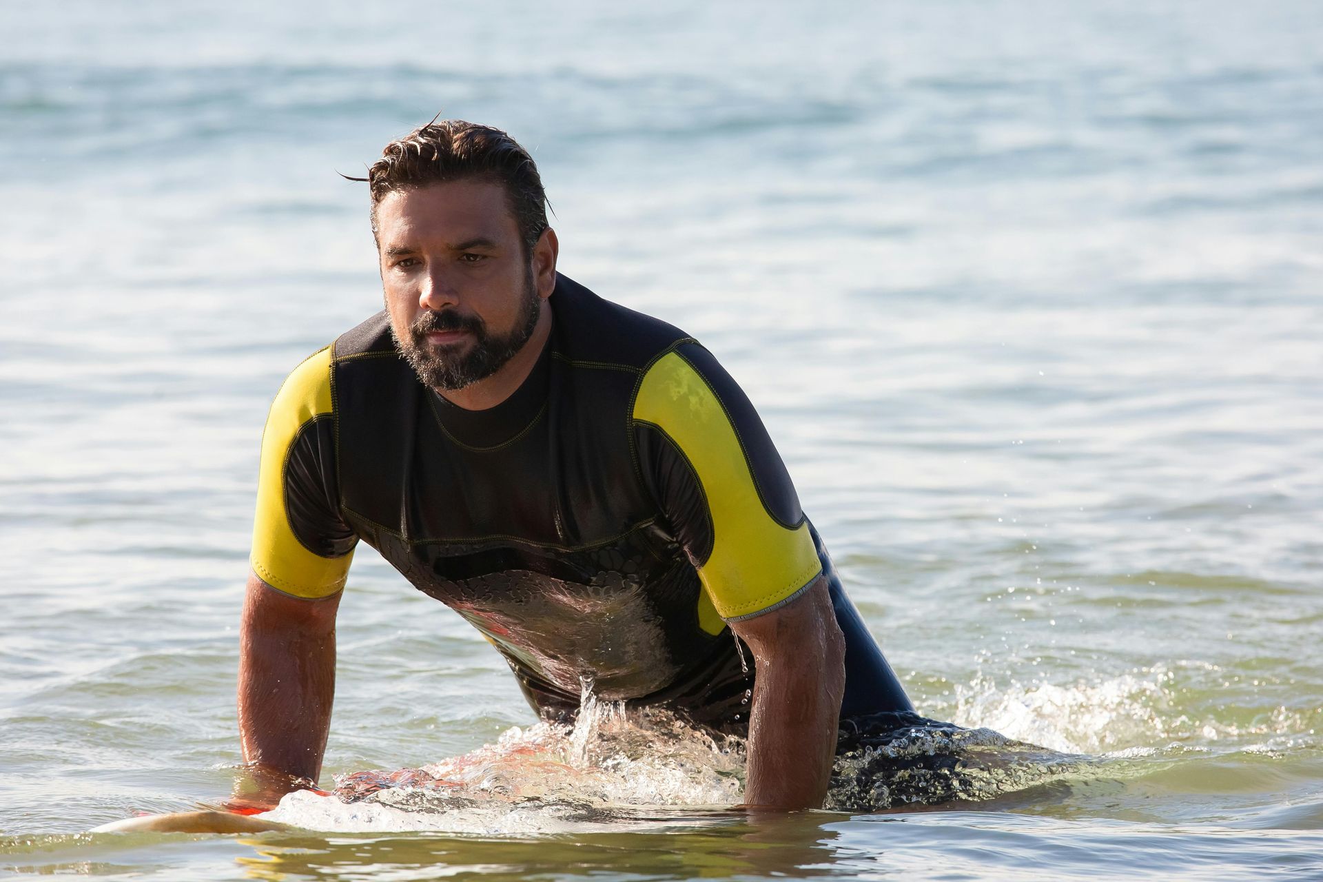 A man in a wetsuit is laying on a surfboard in the ocean.