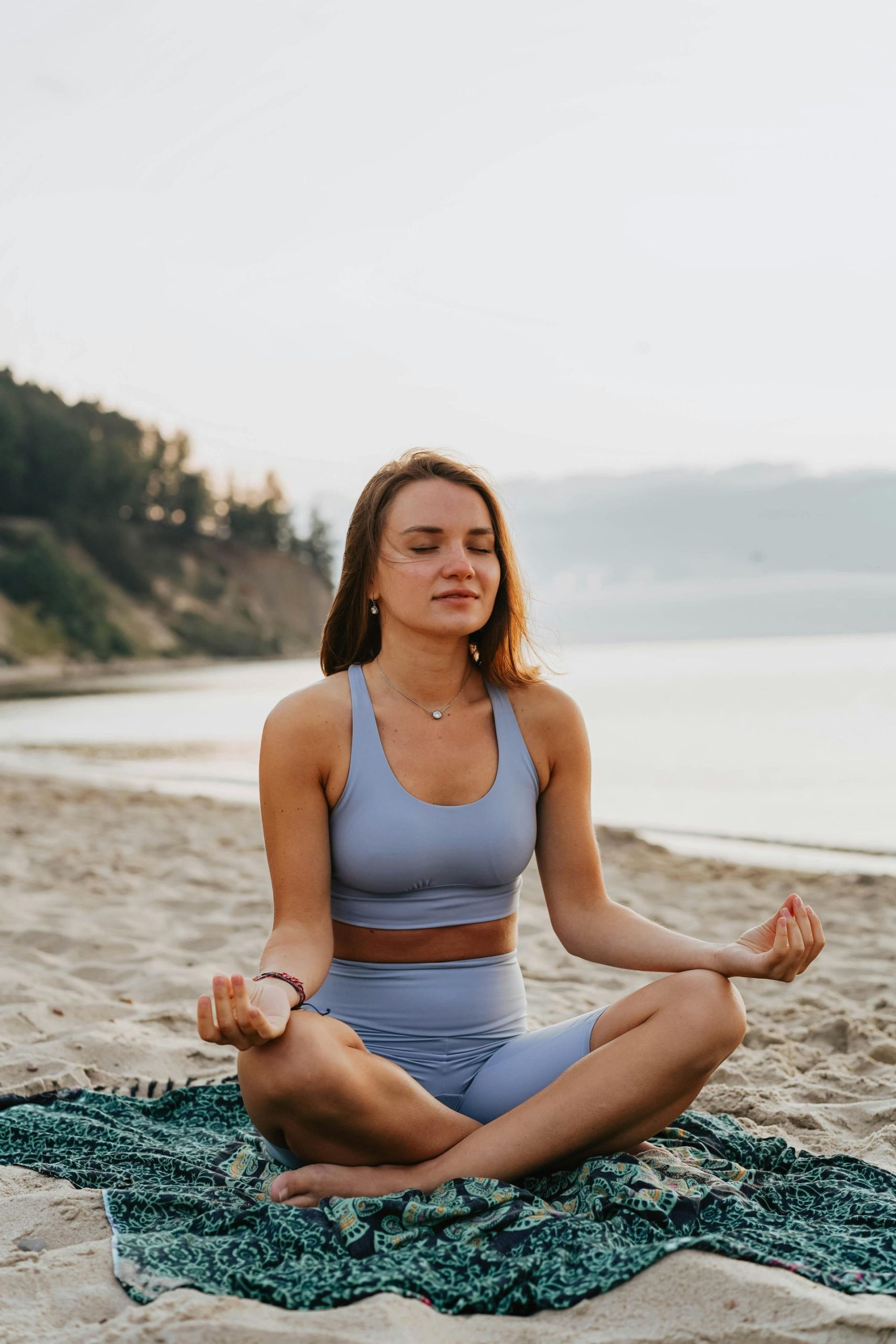 A woman is sitting in a lotus position on the beach.