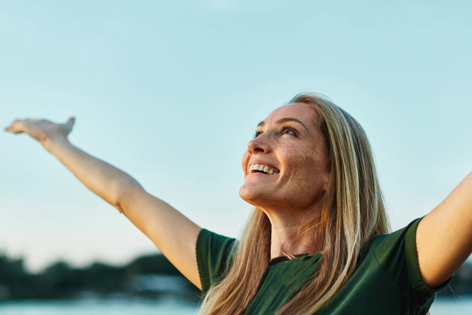 Blonde woman in a green shirt holding her arms up to the sky smiling representing how to stay sober during recovery at California Detox & Recovery Center in Los Angeles.