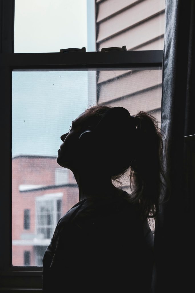 Woman staring out a window wearing headphones pondering the causes and symptoms of alcohol addiction.