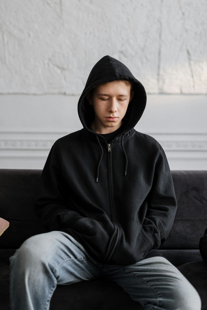 Man in a black hoodie with blue faded jeans sitting on a black couch struggling with the long term effects of methamphetamine addiction in Los Angeles.