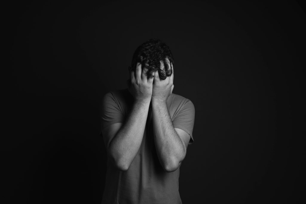 Black and white picture of a man holding both his hands covering his face struggling with opioid addiction.