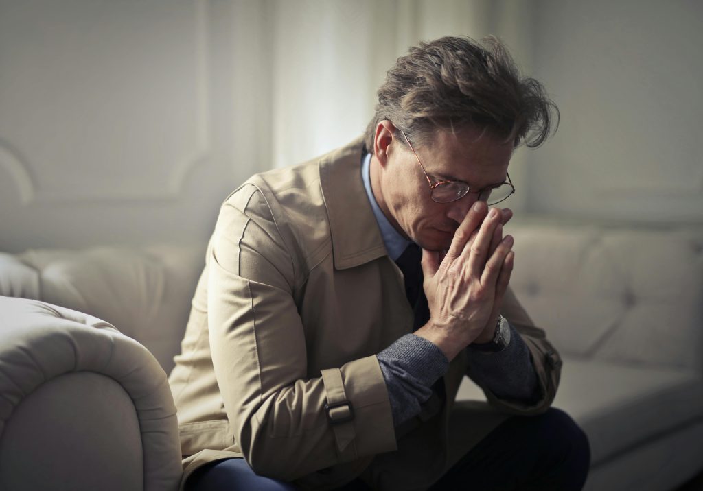 Man holding his hands together in despair struggling with alcohol addiction.