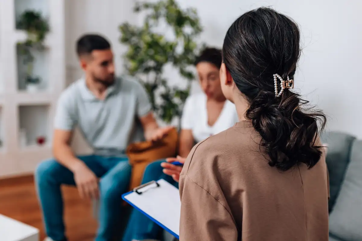 A young female therapist is sitting with her back turned to the camera, while having a couples' counseling session.